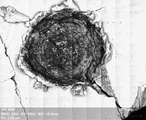 Image au microscope électronique à balayage en électrons rétrodiffusés d’un cratère résultant d’un impact hyper-véloce (5.08 km/s) d’un projectile basaltique sur un morceau de Gibeon, une météorite de fer utilisée comme cible 