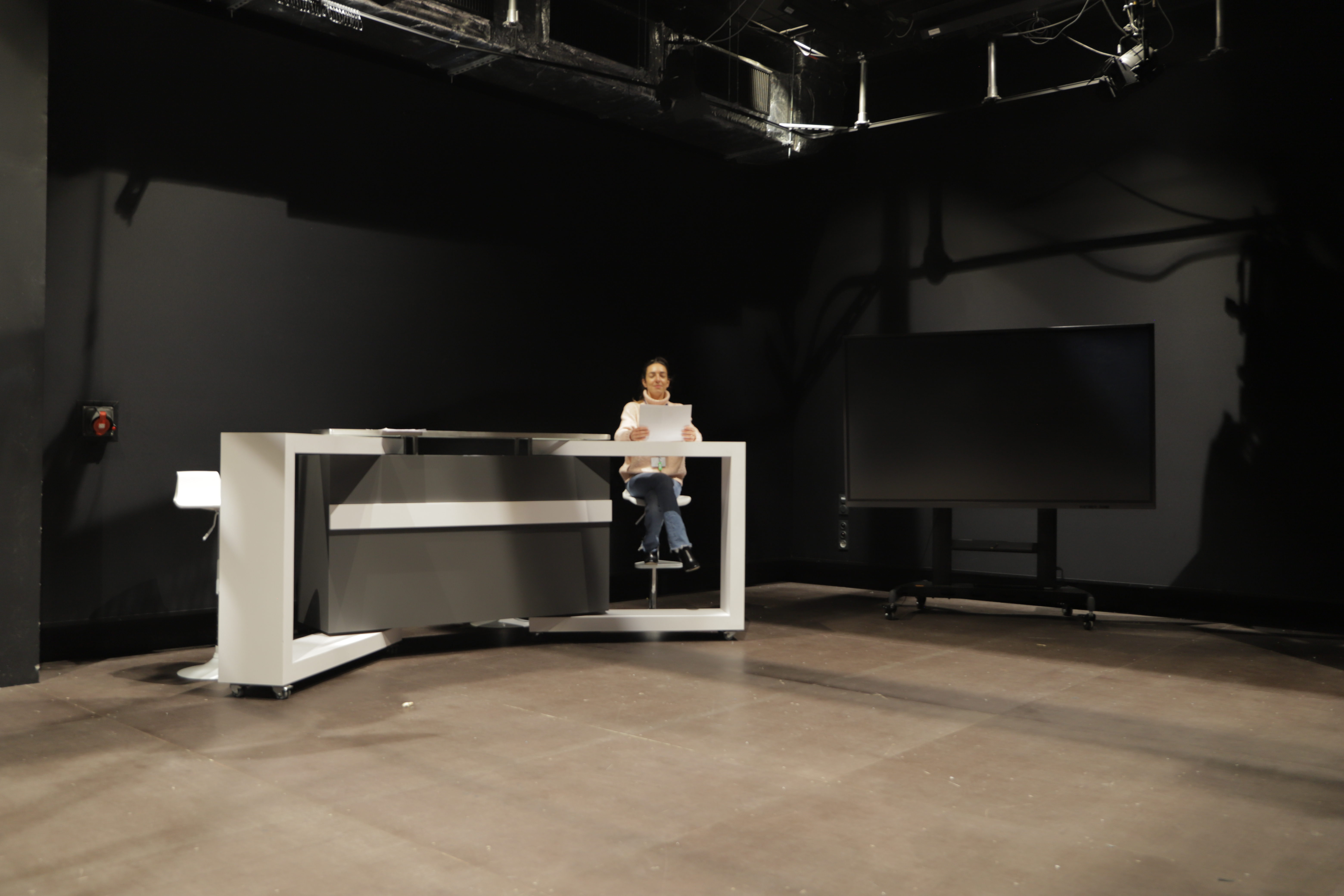 Plateau TV du Campus Georges Méliès à Cannes, équipé d’un bureau de présentation, de tabourets, d’un écran mobile et d’un éclairage scénique. Espace idéal pour tournages, interviews, captations vidéo et projets audiovisuels pédagogiques.