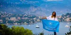 Jeaune femme tenant le drapeau UCA devant un paysage de mer et montagne